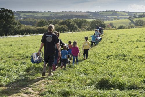Children and adults in Farm School make their way across a beautiful green field at Huxhams Cross Farm